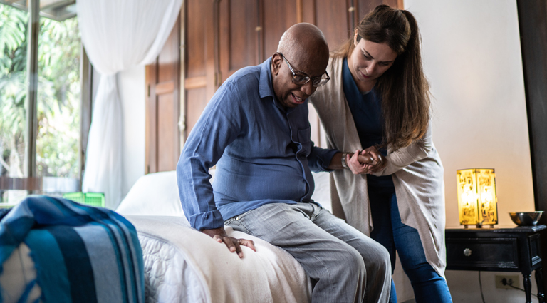 Home caregiver helping a senior man standing up at home